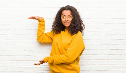 Wall Mural - young black woman holding an object with both hands on side copy space, showing, offering or advertising an object against brick wall