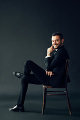 Happy successful man in black suit smiling and looking to camera sitting on the chair