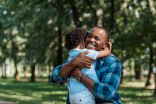 Happy African American Father With Closed Eyes Hugging Curly Son