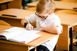 adorable blonde american primary school student with big glasses studying in classroom