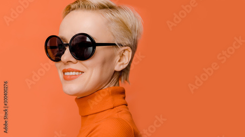 Fotomural Beauty portrait of female model wearing trendy sunglasses over orange background