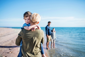 Young family with two small children walking outdoors on beach.