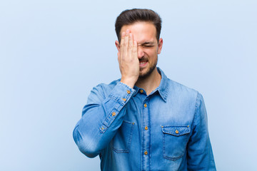 young handsome man looking sleepy, bored and yawning, with a headache and one hand covering half the face