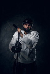 Professional hockey player in helmet is posing with hockey stick at photo studio.