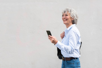 Wall Mural - happy older woman walking with handbag and cellphone by white background