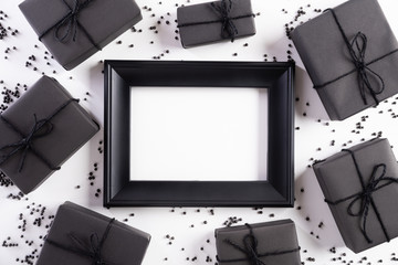 Top view of Black Friday Sale text on white picture frame with black gift box and Christmas ball and berries on white background. Shopping concept and black Friday composition.