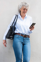 Wall Mural - smiling older woman with bag looking at cellphone