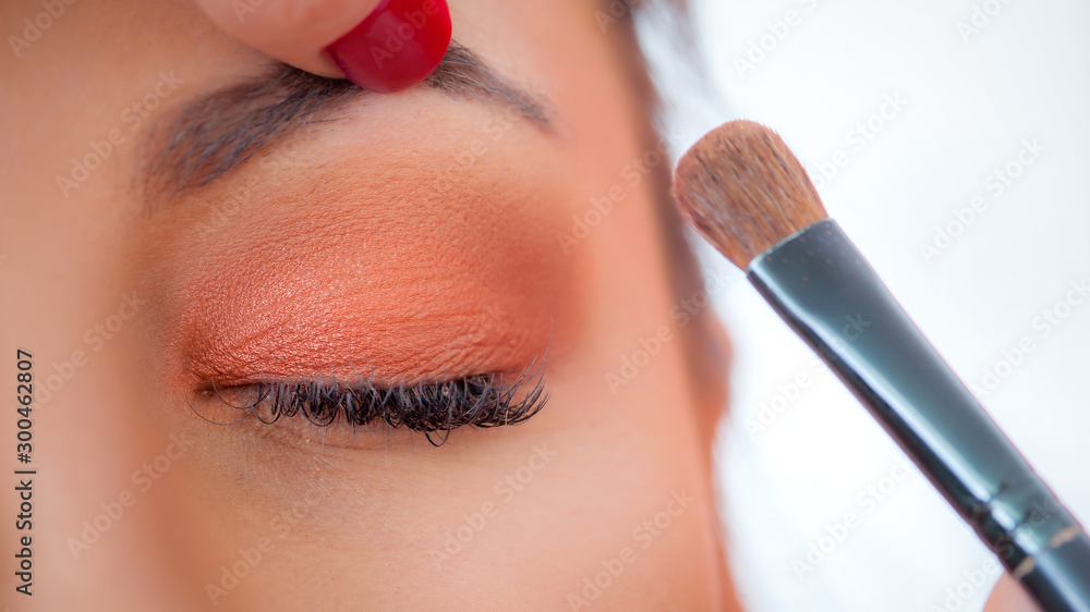 Makeup professional artist applying base color eyeshadow on model eye - obrazy, fototapety, plakaty 