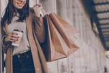 Fototapeta Boho - Beautiful fashionable woman drink coffee walking near mall with shopping bags.