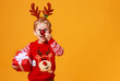 © JenkoAtaman - happy funny child boy in red Christmas reindeer costume with gift on yellow   background