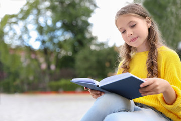 Wall Mural - Cute little girl reading book in green park