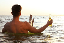 Young Man With Drink On Inflatable Ring In Sea, Back View