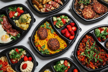 Lunchboxes with different meals on white table, flat lay. Healthy food delivery