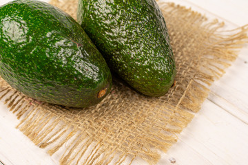 Group of two whole fresh green avocado on natural sackcloth on white wood