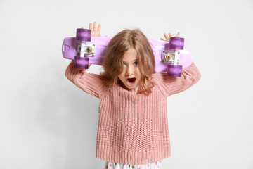 surprised little girl with skateboard on light background