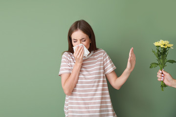 Wall Mural - Young woman with allergy refusing to take bouquet on color background