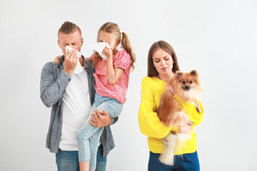 Wall Mural - Young woman with dog and husband with daughter suffering from pet allergy on light background