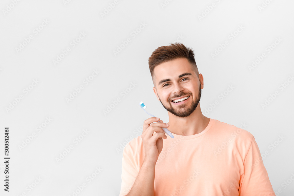 Portrait of man brushing teeth on light background