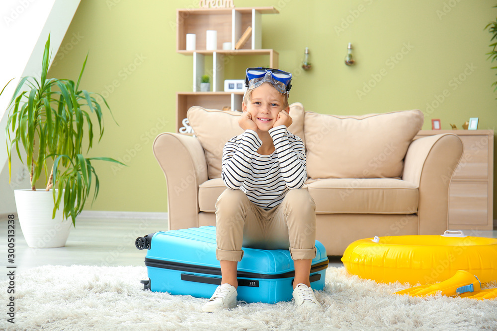 Cute little boy sitting on suitcase at home