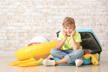 Poster - Cute little boy and suitcase with things for summer vacation near brick wall