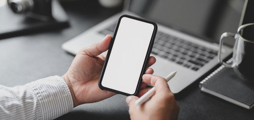 Canvas Print - cropped shot of professional businessman holding blank screen smartphone in dark modern office