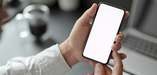 Canvas Print - cropped shot of professional businessman holding blank screen smartphone in dark modern office
