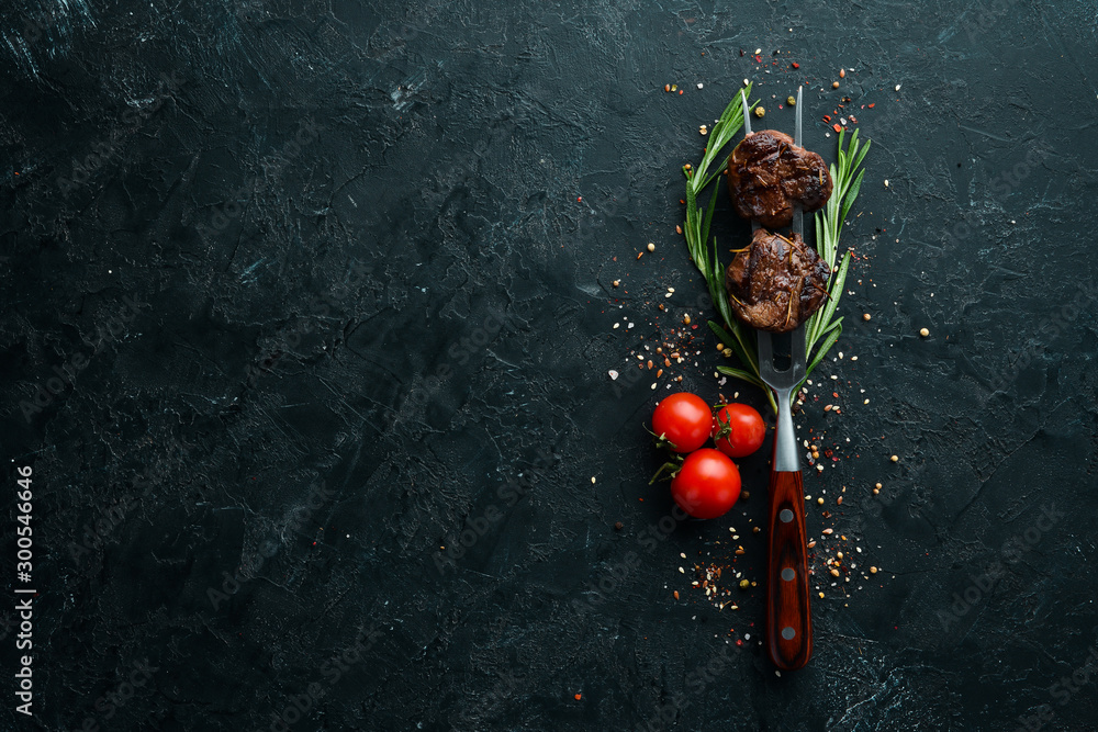Baked veal on a fork. Veal steak on black stone background. Top view. Free space for your text. - obrazy, fototapety, plakaty 