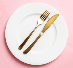 Gold cutlery and dishes set against pink background, formal place setting