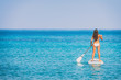 Paddle board bikini woman standing paddling away on stand up paddleboarding on ocean blue background water. Hero view of girl standing on sup surfboard watersport leisure activity.