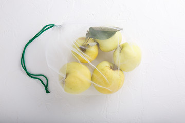 Apples in textile grocery mesh bag. Yellow fruits and vegetables in reusable eco friendly packaging on white background.