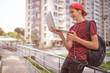 © Valua Vitaly - Smiling teenage boy with a laptop on the street. Handsome young man works on a notebook, outdoors. Cheerful guy holds a laptop on the knees and looking to screen. Teenager in headphones with laptop