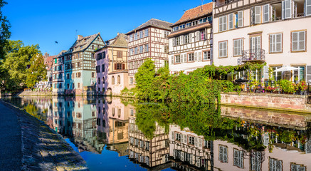 Wall Mural - Panoramic view of the half-timbered houses lining the canal of the river Ill in the Petite France quarter in Strasbourg, France, reflecting in the still waters on a sunny morning.