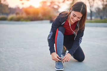 Young modern woman tying running shoes in urban park.