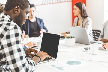 A team of young office workers, businessmen with laptop working at the table, communicating together in an office. Corporate businessteam and manager in a meeting. coworking.