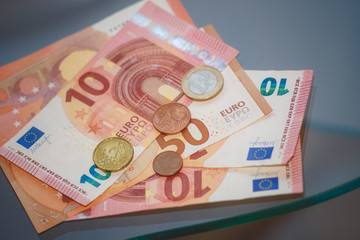 A few Euro bills and coins lie on a glass table.