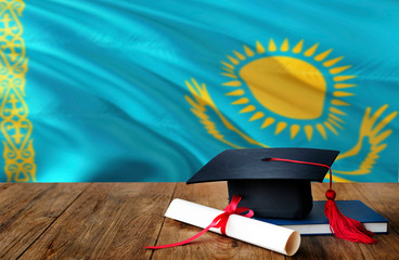 Kazakhstan education concept. Graduation cap and diploma on wooden table, national flag background. Succesful student.