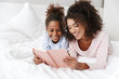 © Drobot Dean - Image of african american woman and her little daughter reading book in bed