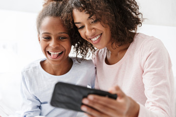 Wall Mural - Image of american woman and little daughter taking selfie at home