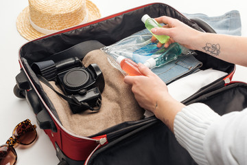 cropped view of woman packing travel bag with cosmetic bag with colorful bottles