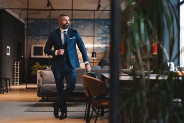 Wall Mural - Stylish bearded man in a suit standing in modern office