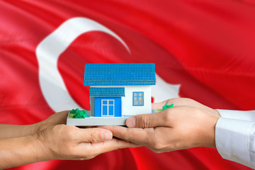 Turkey real estate concept. Man and woman holding miniature house in hands. Citizenship theme and national flag on background.