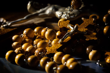 Jesus Christ catholic crucifix and wooden rosary beads under beam of light