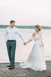 © pavelvozmischev - Stylish European wedding at sunset. Happy couple on the pier on the lake.