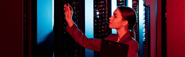 panoramic shot of businesswoman holding clipboard and looking at server room