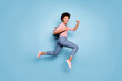 Full length photo of cheerful funny teenage afro american girl jump run college hold backpack wear striped shirt denim jeans pink sneakers isolated over blue color background