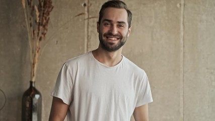 Poster - Attractive cheerful young brunet man smiling while looking at the camera at home