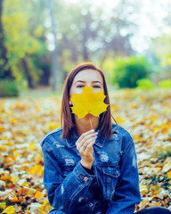 Wall Mural - Women is holding autumn leaf and is lying on the floor facing sky. There are also dried brown autumn leaves surrounding her.