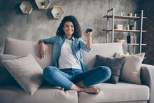 Photo Of Pretty Dark Skin Wavy Lady Homey Mood Holding Tv Remote Control Changing Channel Searching Favorite Humor Show Sitting Comfy Couch Casual Denim Outfit Flat Indoors