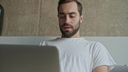 Sticker - Close up view of handsome serious young brunet man becoming angry and tired while working on laptop sitting on couch at home