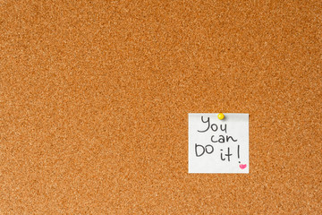 You can do it! Handwritten inspirational supportive lettering on a sticker on a cork board. Background and texture.